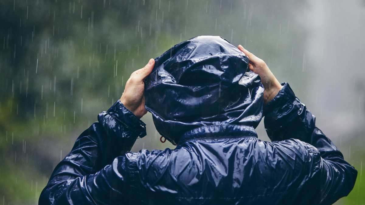 Man wearing raincoat walking through woods as a rain storm is happening.